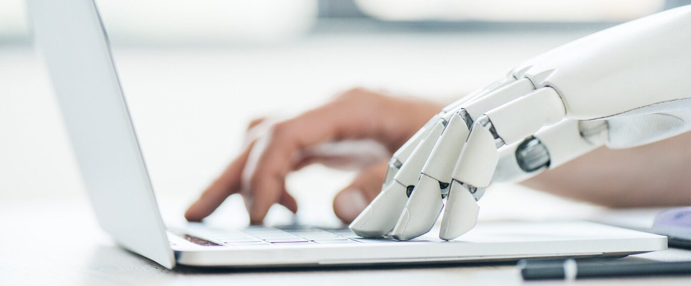 Roboterhand und menschliche Hand tippen gleichzeitig auf Tastatur.