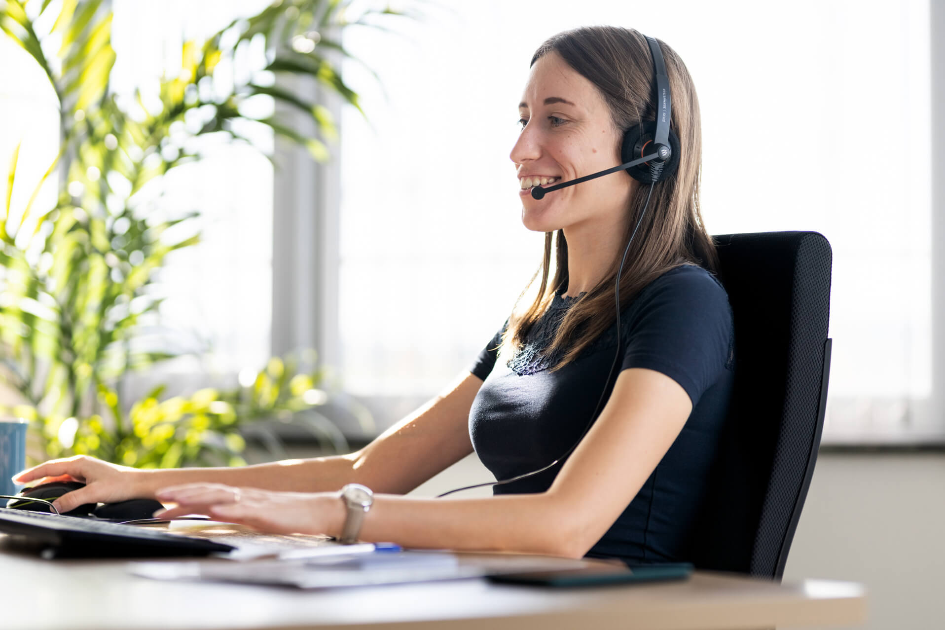 Lektorin sitzt lächelnd mit Headset an Schreibtisch in modernem Büro.