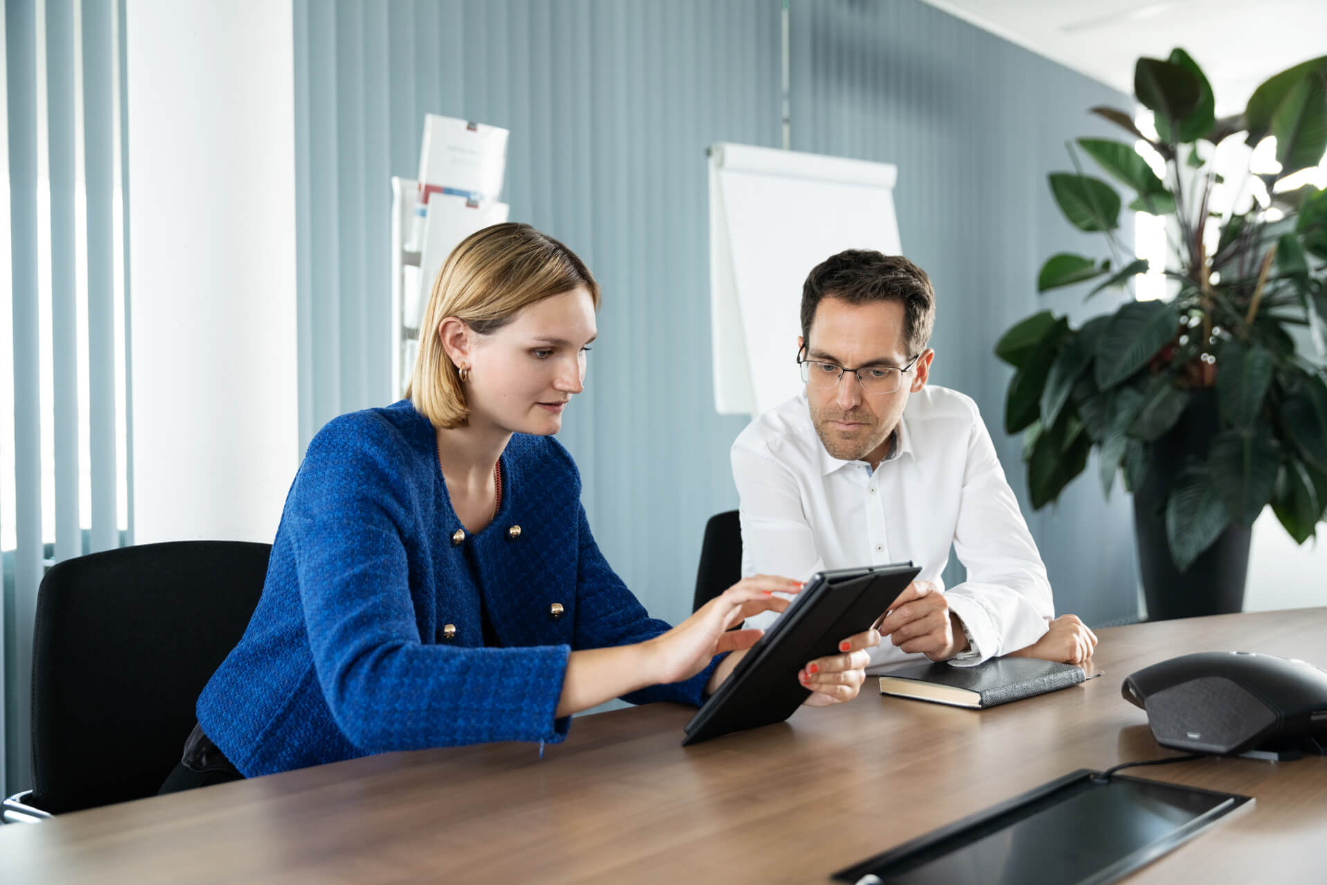 Female technical author sitting next to her colleague with a tablet at a conference table.