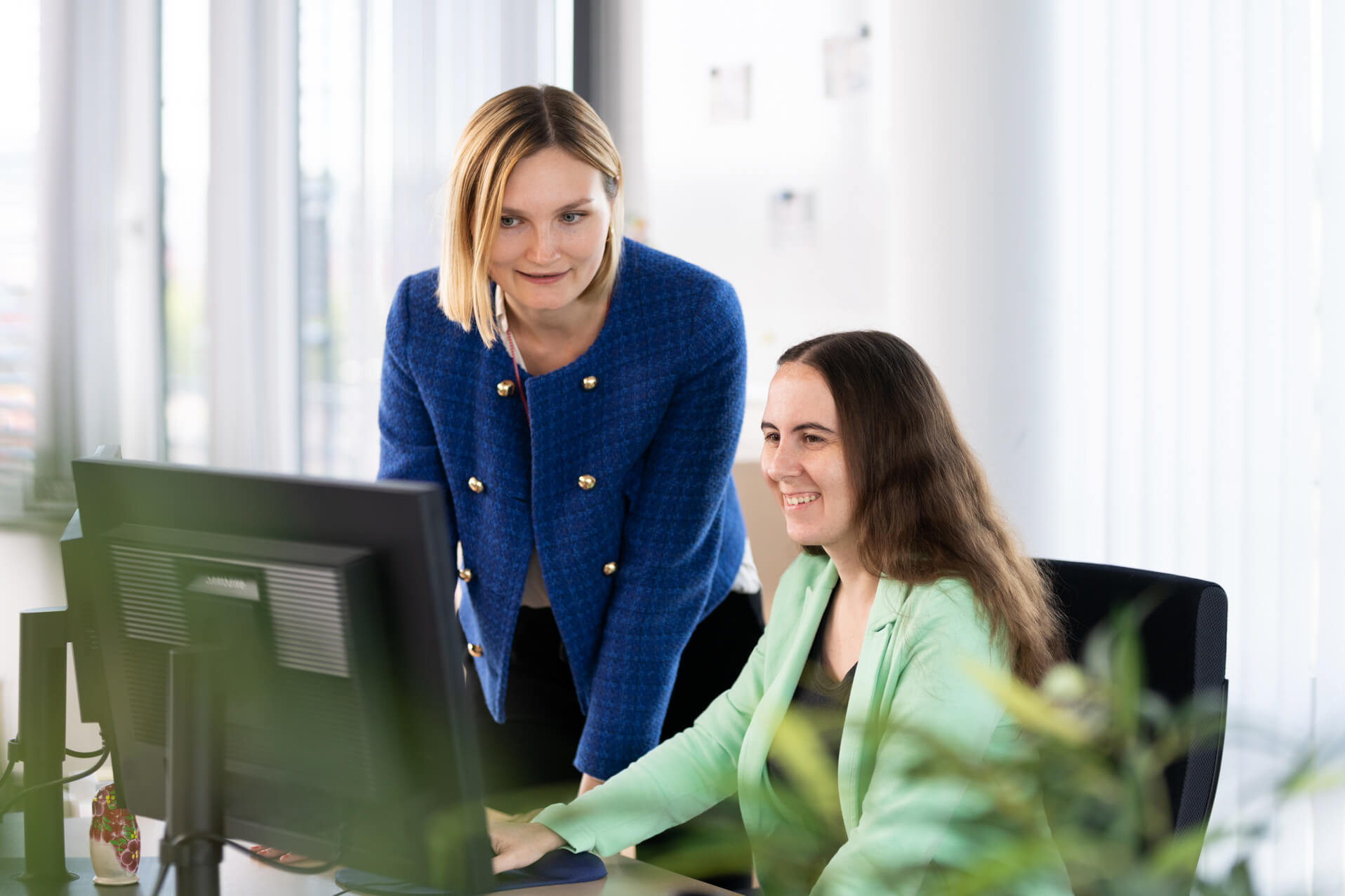 Zwei Kolleginnen schauen gemeinsam nach Lokalisierungssoftware auf einen Monitor.