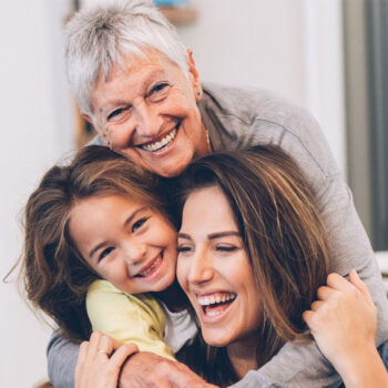 Drei Generationen Mammotome Kundinnen - Mutter, Tochter und Enkelin umarmen sich und lachen.