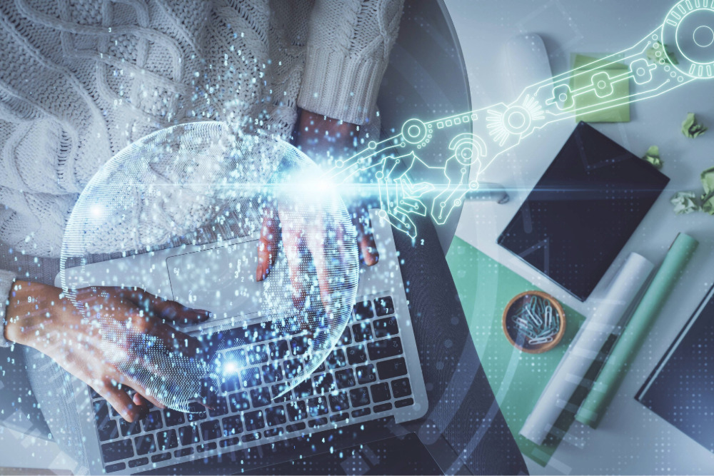 Person tippt am Laptop, daneben digitale Roboterhand – Symbol für KI in Sprachprozessen.