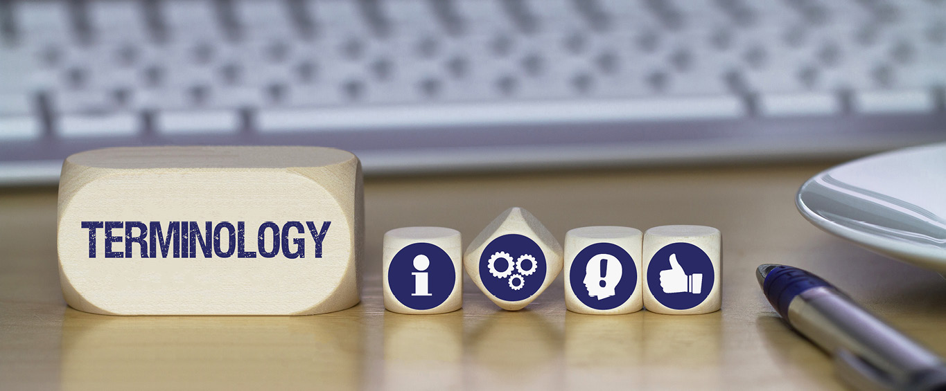 Symbolbild zur Terminologiearbeit mit Künstlicher Intelligenz – Holzklötze mit dem Wort „TERMINOLOGY“ und Symbolen für Information, Prozesse, Warnhinweise und Zustimmung auf einem Schreibtisch mit Tastatur und Stift.