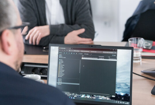Laptop mit geöffnetem Dateiordner während einer Arbeitsbesprechung zur technischen Dokumentation.