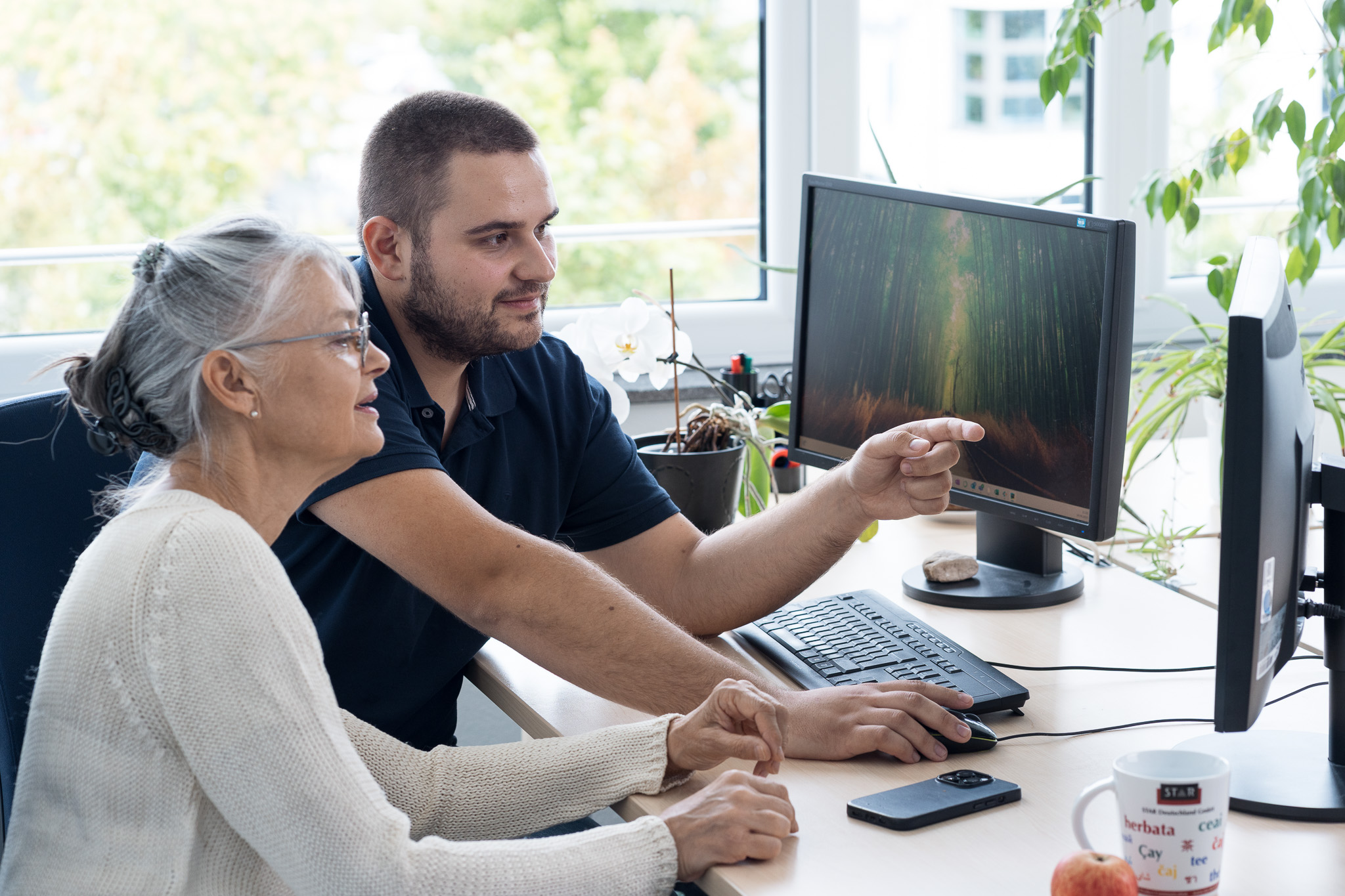 Two people sitting at a desk reviewing content on a computer screen together.