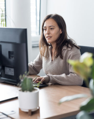 Person arbeitet an einem Computerarbeitsplatz in einem Büro mit Pflanzen im Hintergrund.