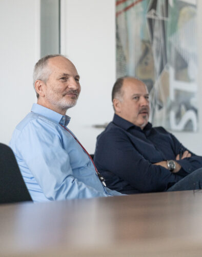 Two people sitting in a meeting room listening to a presentation or discussion.