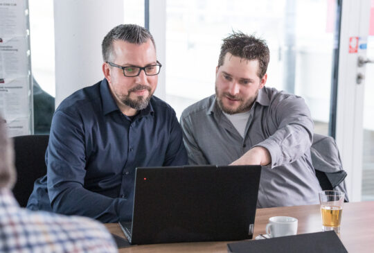 Zwei Personen arbeiten gemeinsam an technischen Dokumentationsinhalten an einem Laptop.